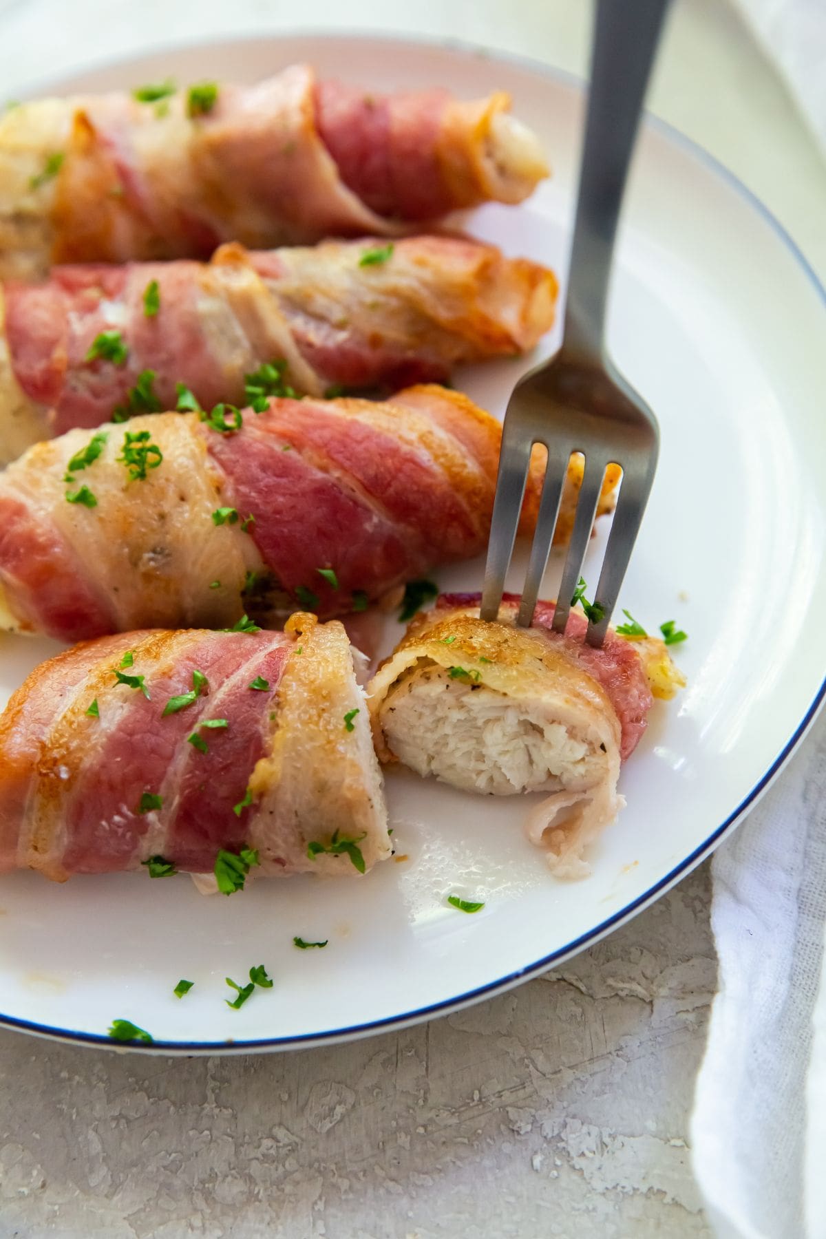 Bacon wrapped chicken tenders one piece cut with a fork in it.