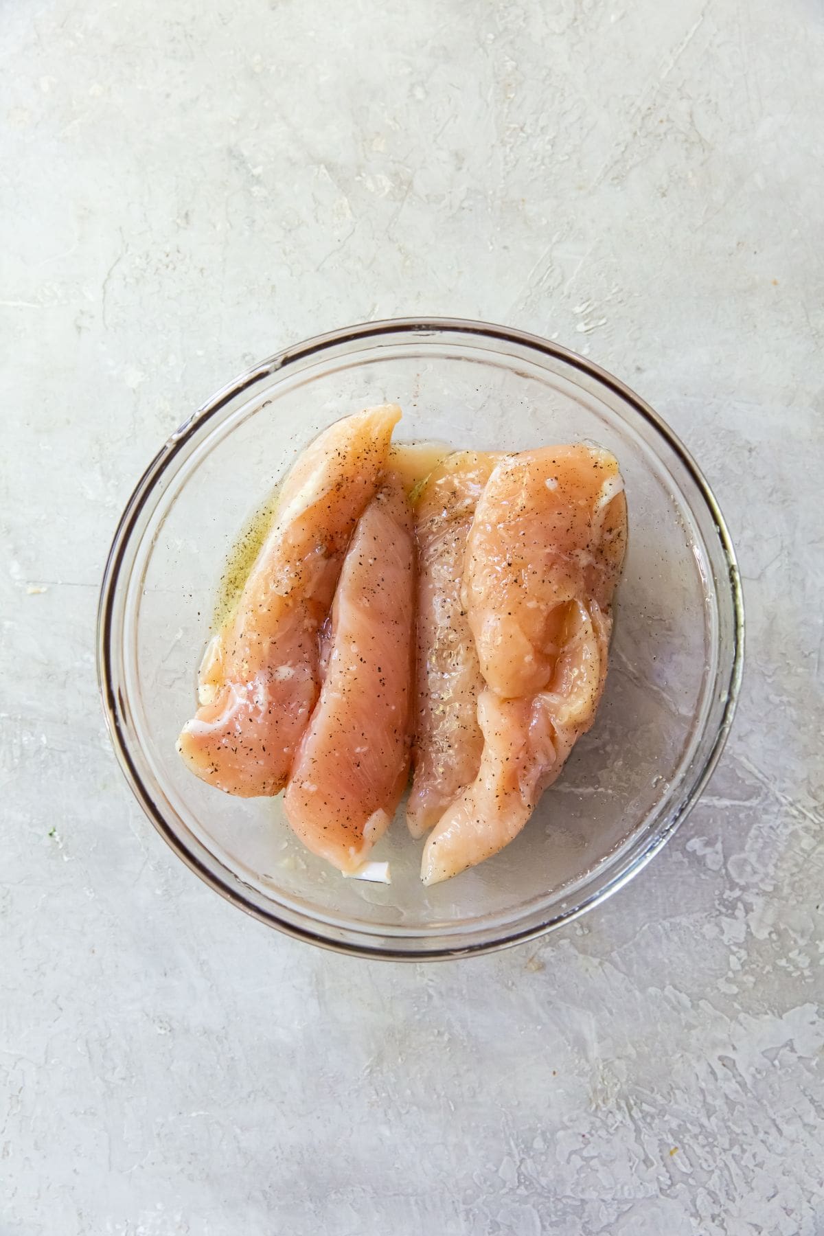 Glass mixing bowl with chicken tenders tossed in ingredients.