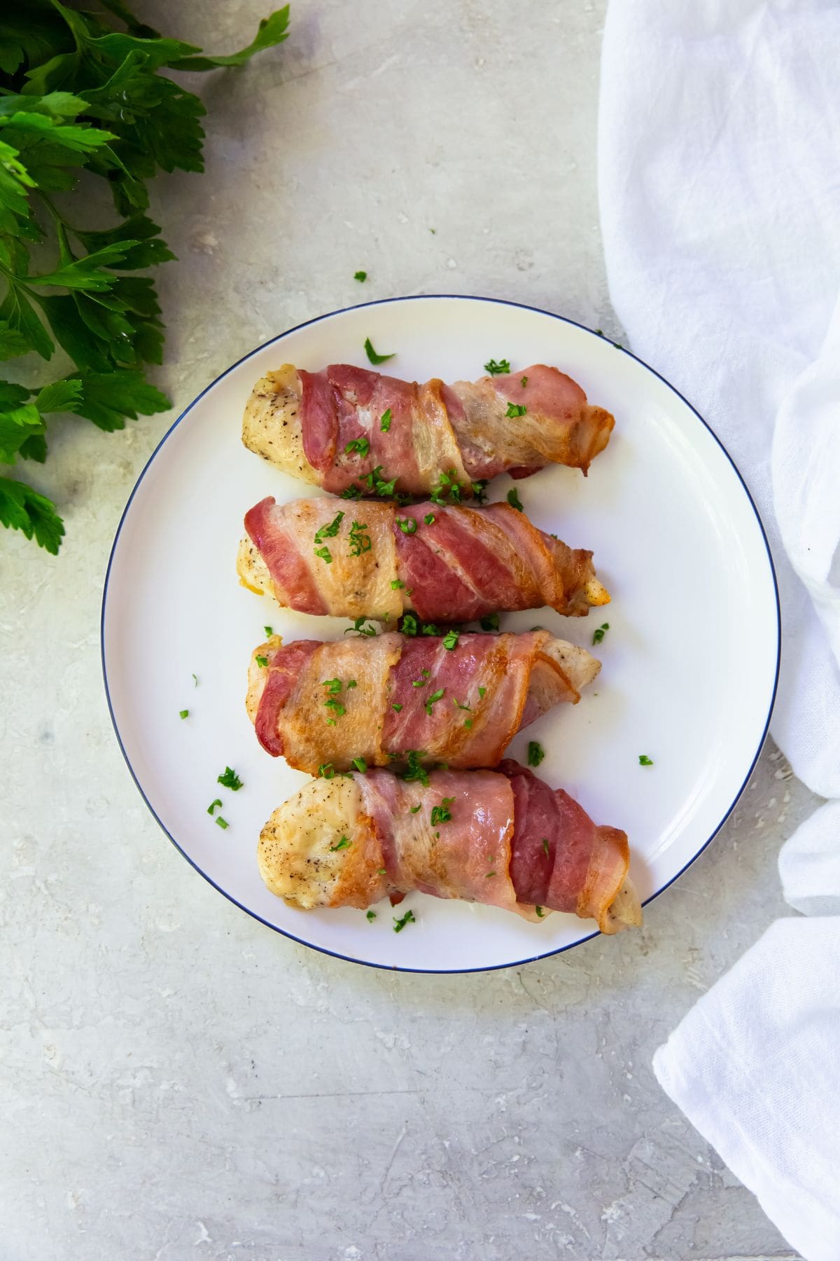 bacon wrapped chicken tenders on a white plate. parsley top left corner. white towel on side