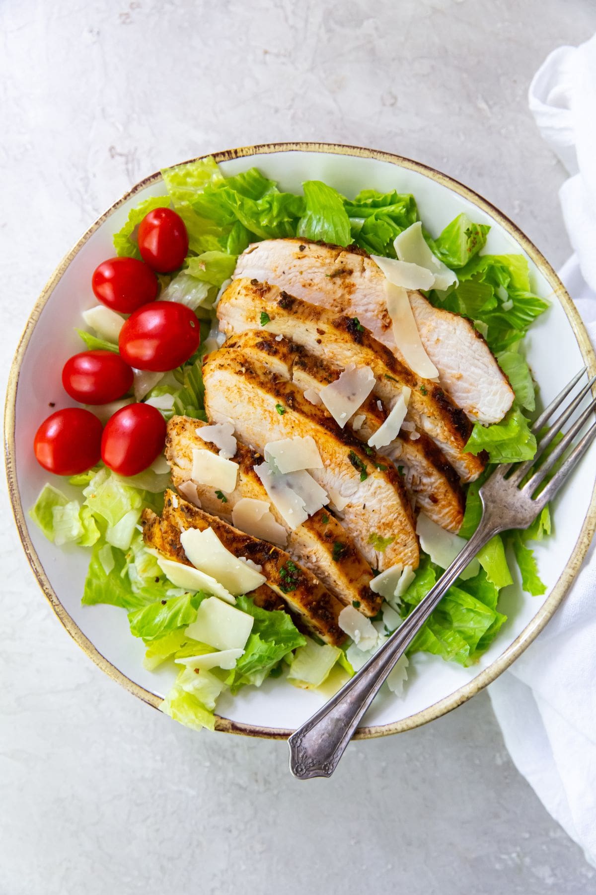 bowl with lettuce, tomato and parmesan cheese with sliced blacked chickened on top 