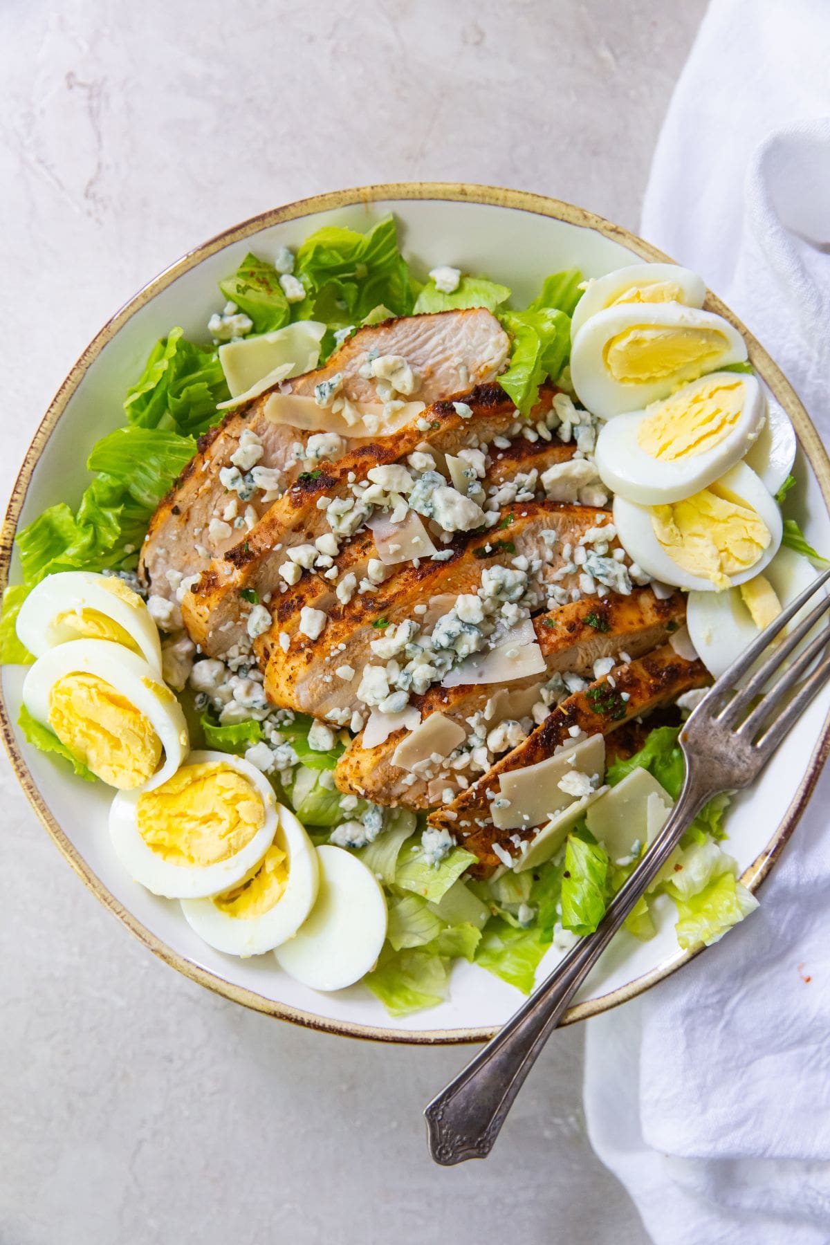 bowl with salad in blacked chickened on top with hard boiled eggs and blue cheese crumbles for on side