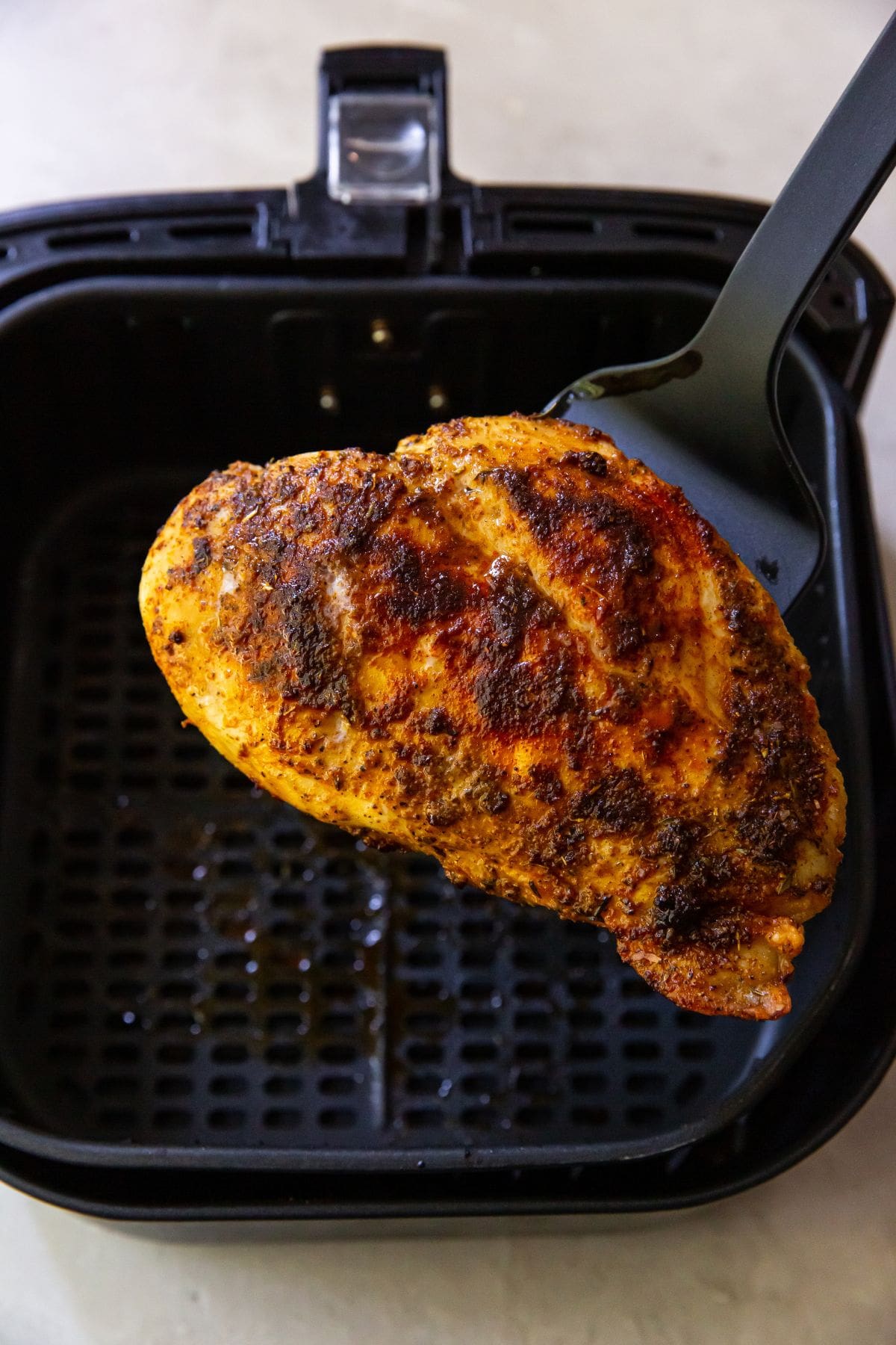 cooked chicken breast being held up by spatula