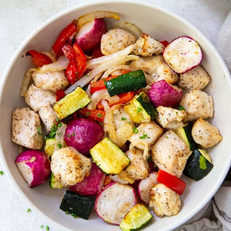 White bowl with chicken and veggies inside it. Gray towel on side