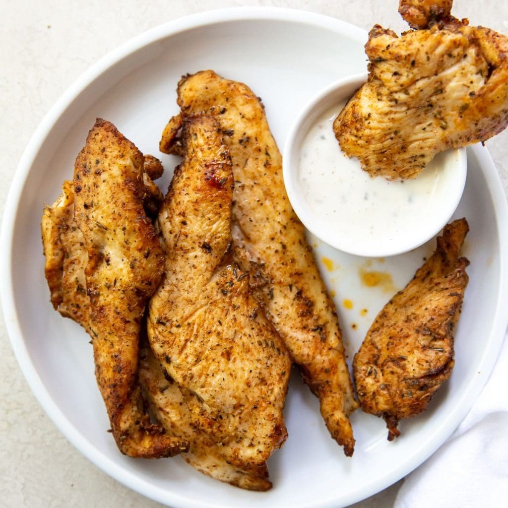 chicken breast strips on a white plate being dipped into ranch