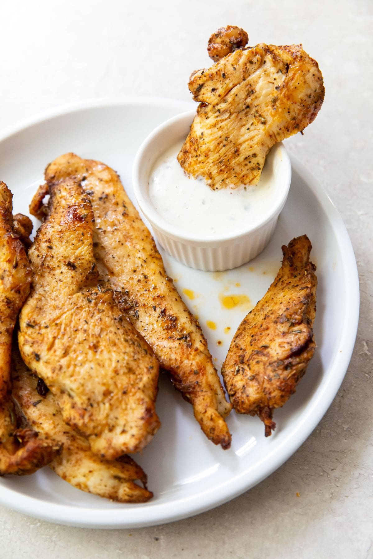 Gray background with white plate chicken breast tenders. One dipped into a side dish of ranch