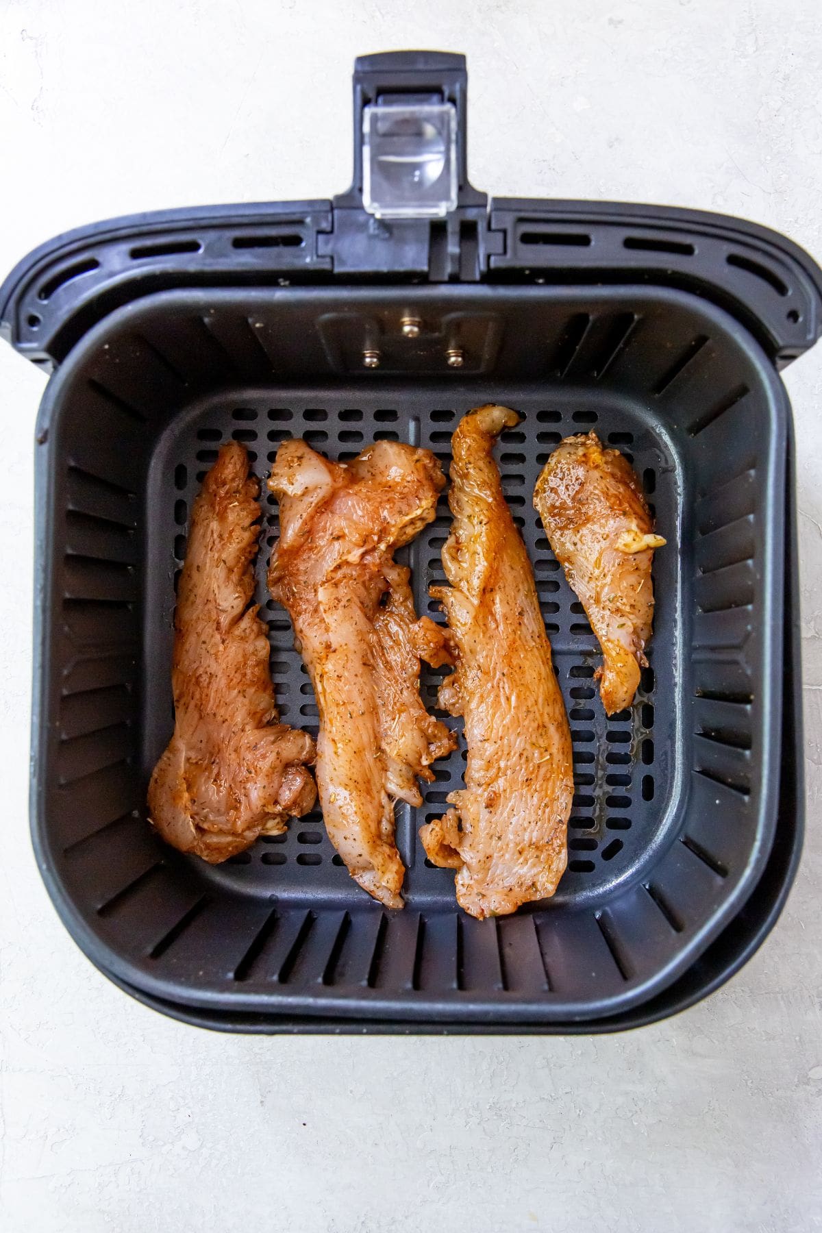 Black air Fryer with 4 uncooked chicken breast strips inside 