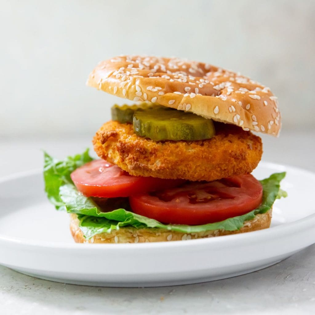 Gray background with white plate. has chicken patty on the plate with lettuce, tomato, and pickles