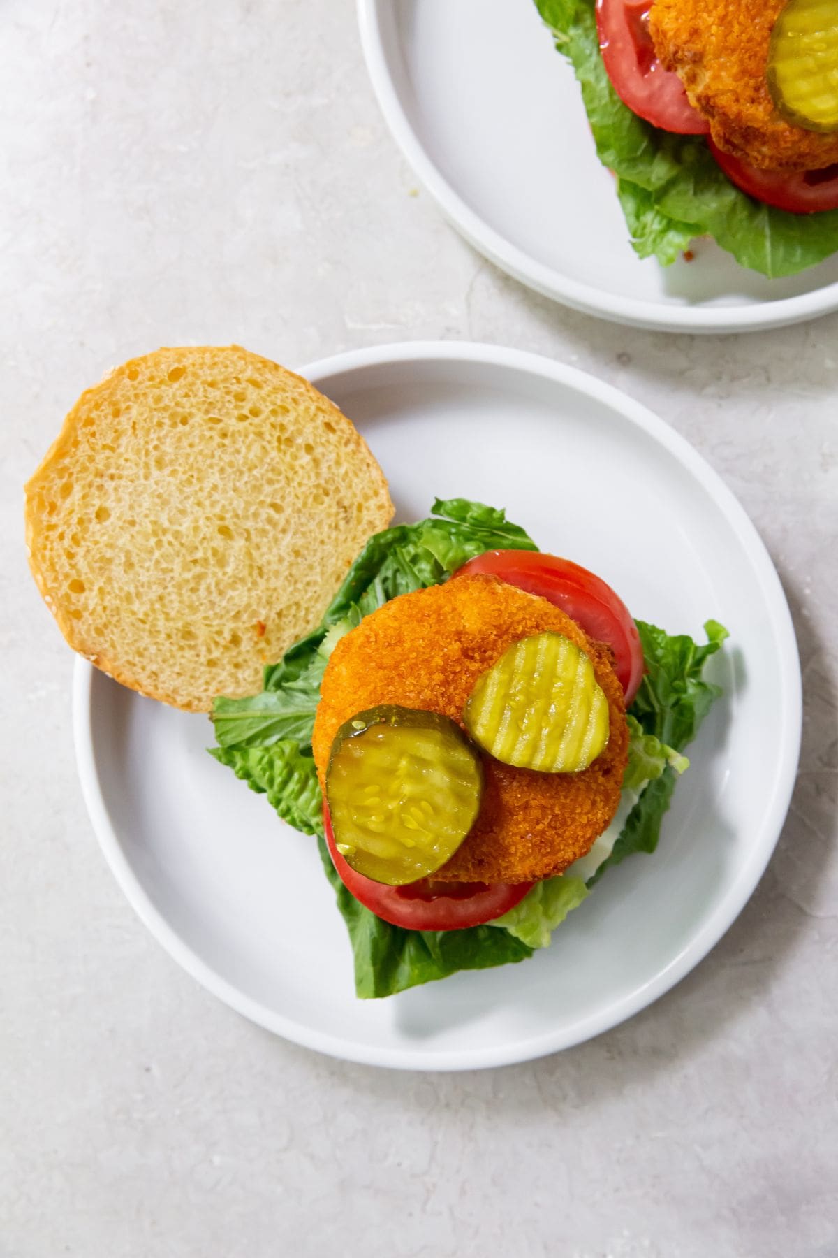 White plate with Hamburger bun that has tomato lettuce chicken patty and pickles