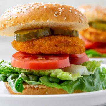 White plate with Hamburger bun that has tomato lettuce chicken Pattie and pickles