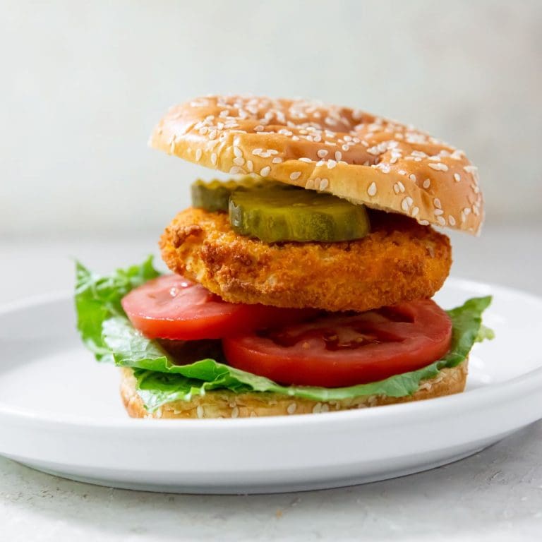 Gray background with white plate. has chicken patty on the plate with lettuce, tomato, and pickles