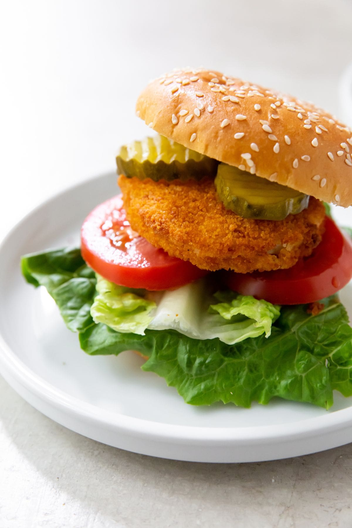 White plate with Hamburger bun that has tomato lettuce chicken patty and pickles