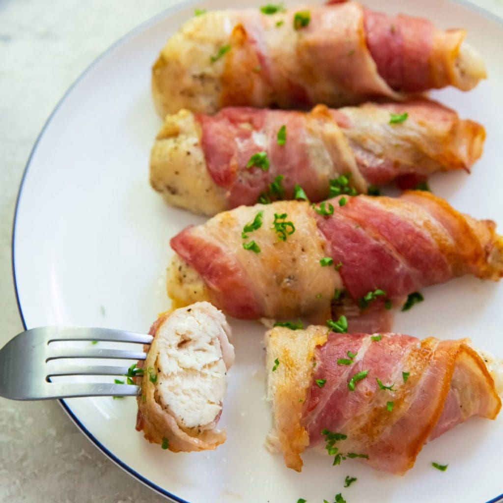 Bacon wrapped chicken tenders one piece cut with a fork in it.