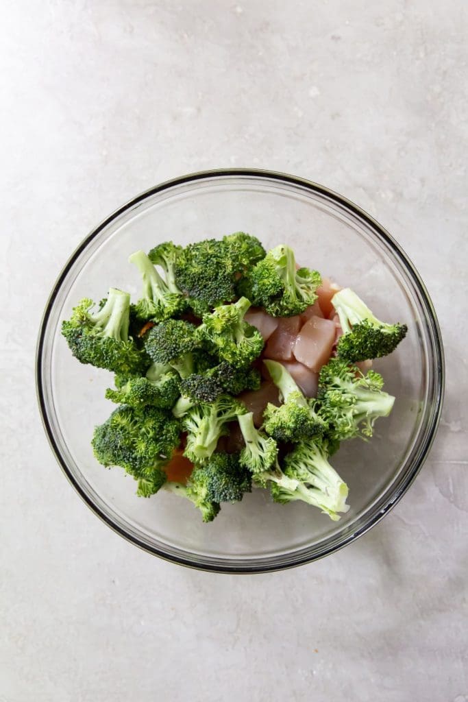 Gray background with glass bowl. Chicken and broccoli sitting on top of ingredients