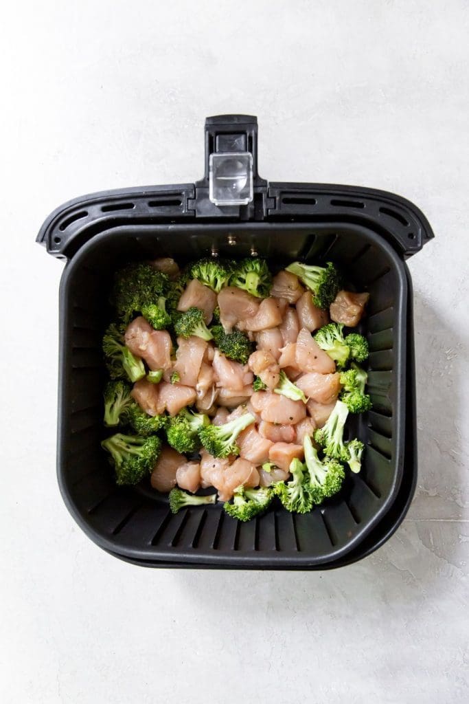 Black Air fryer with raw chicken and broccoli