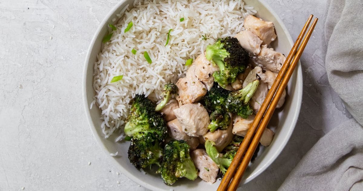 chicken and broccoli in a white dish with rice an chopsticks