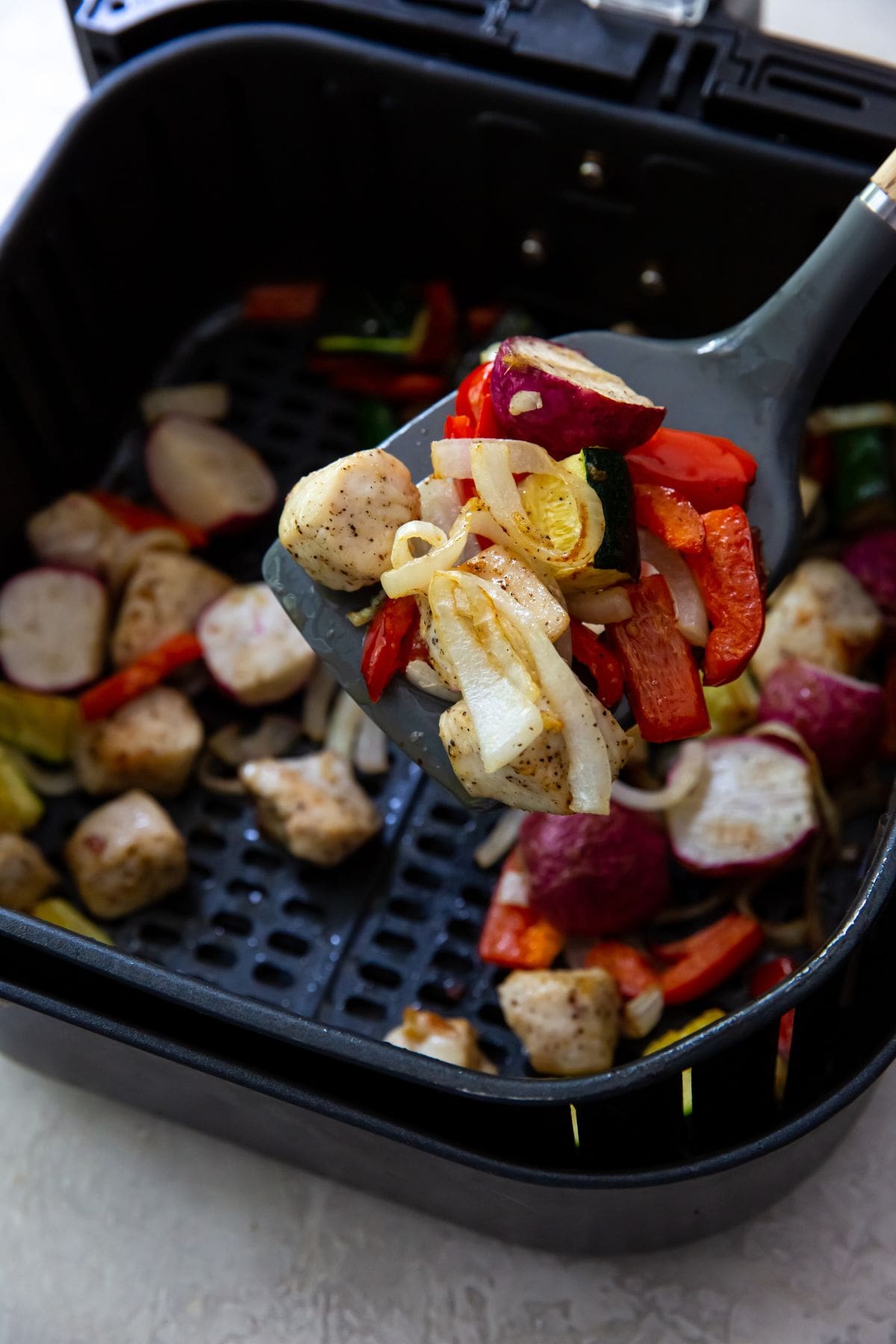 Black Air Fryer with spatula holding chicken and veggies