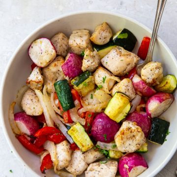 White bowl with chicken and veggies inside it. Fork inside the bowl on the side