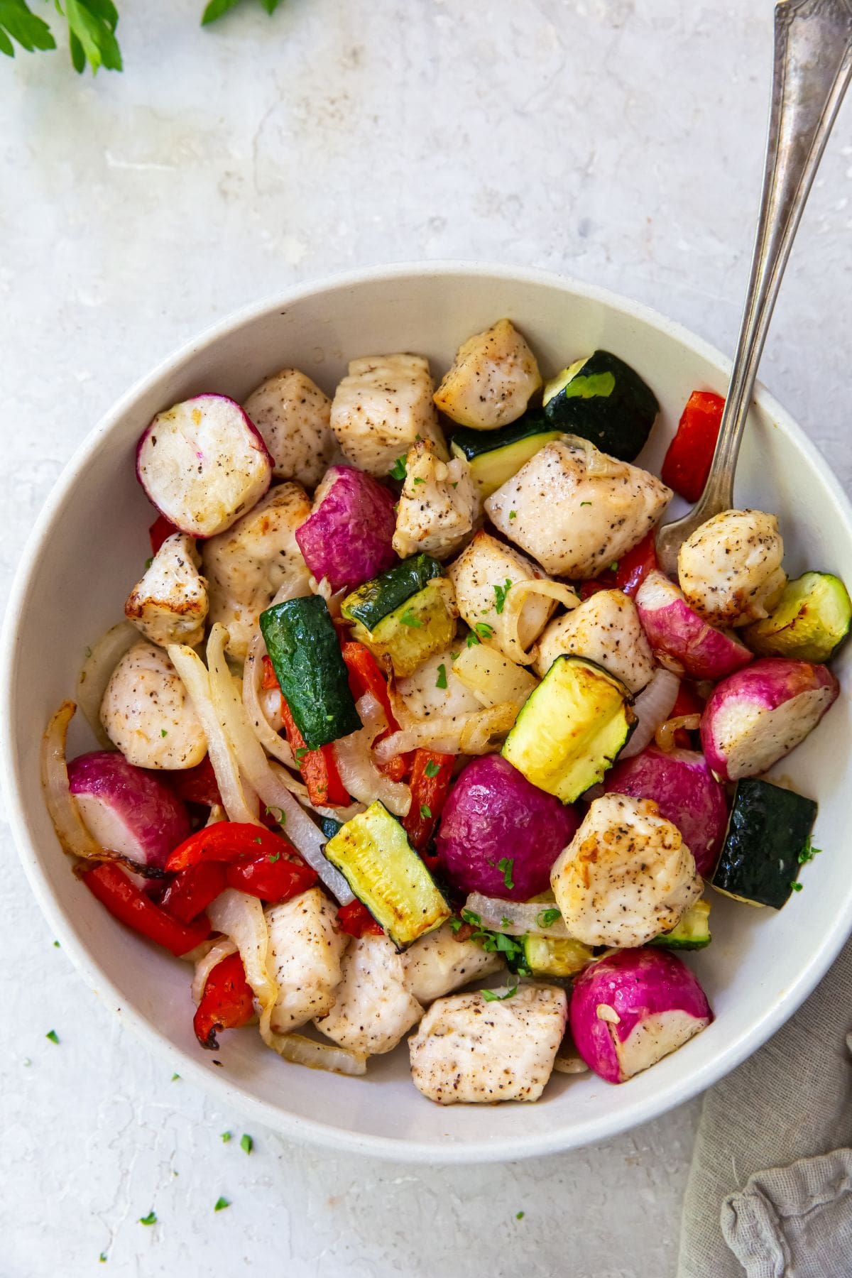 White bowl with chicken and veggies inside it. Fork inside the bowl on the side