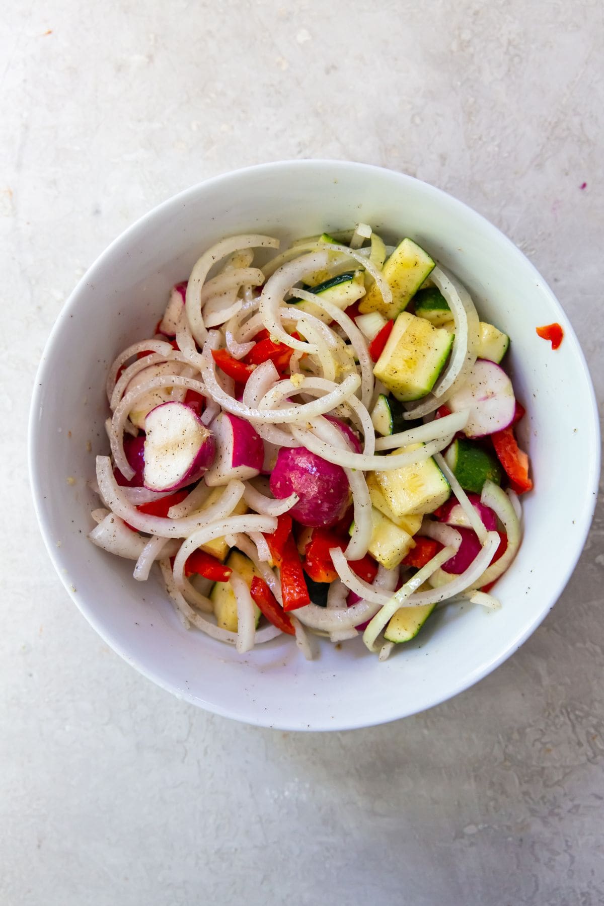 All the veggies in a white bowl with salt, pepper, avocado oil, and garlic mixed together