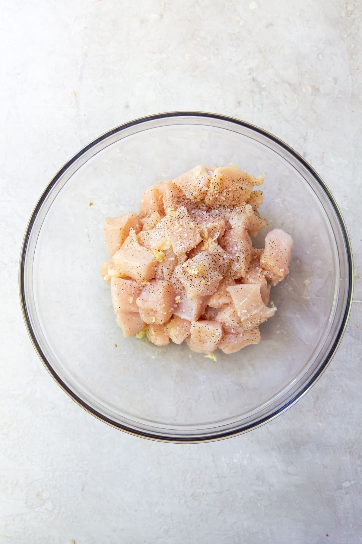 Glass bowl with chicken, salt, pepper, garlic, and avocado in it