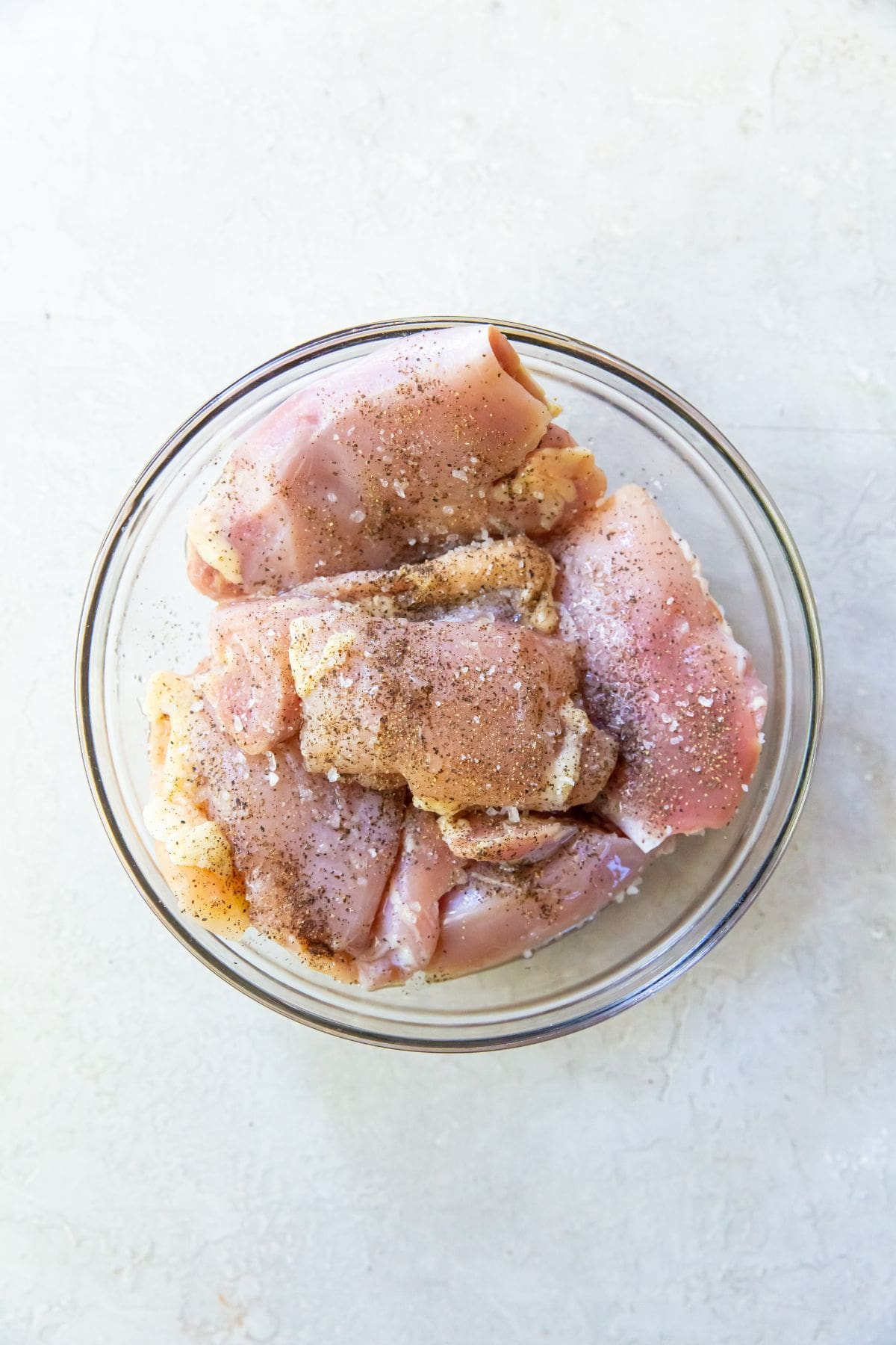 Glass bowl with chicken thighs and seasonings on top