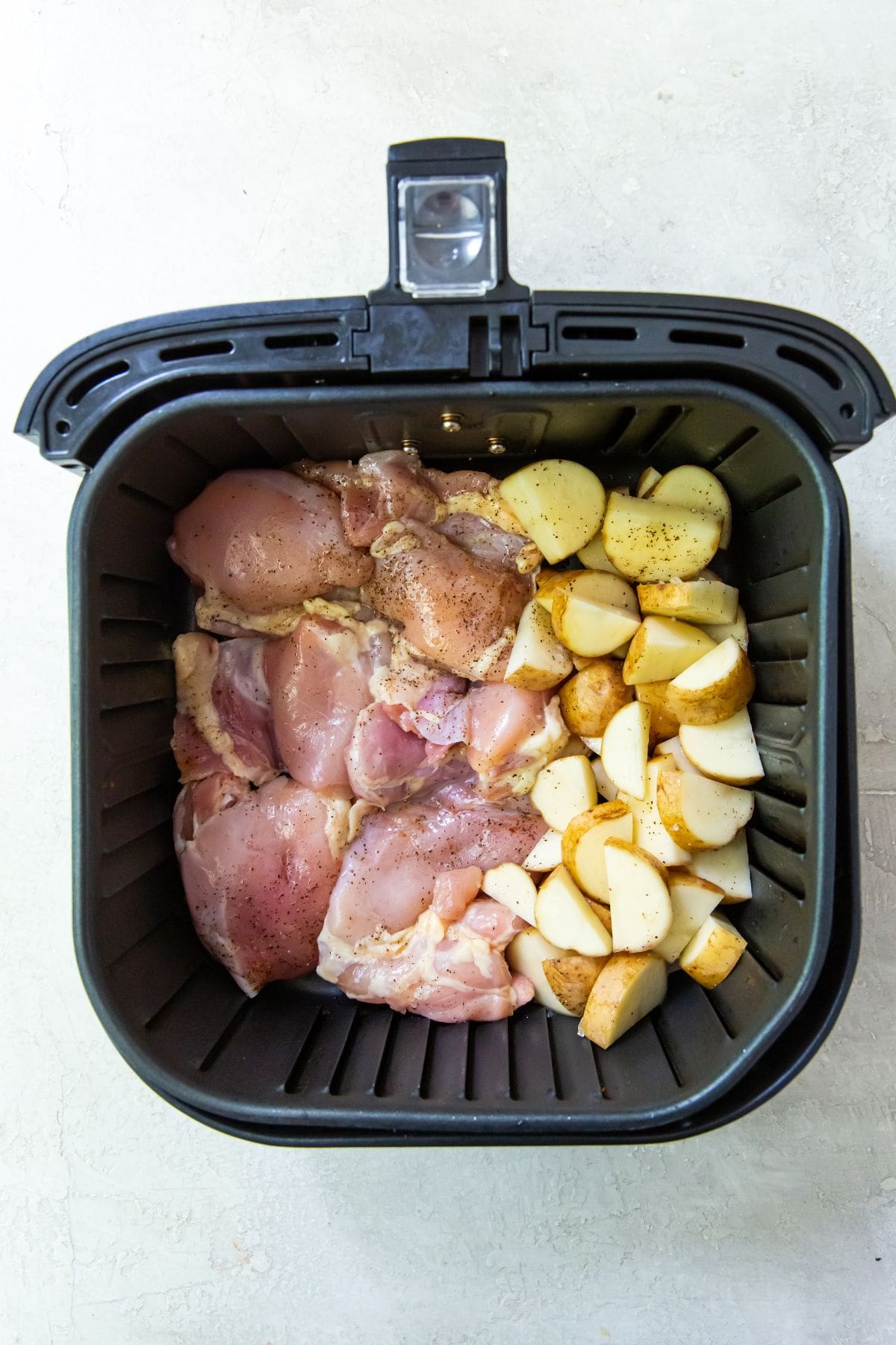 uncooked chicken thighs and potatoes in a Air Fryer.