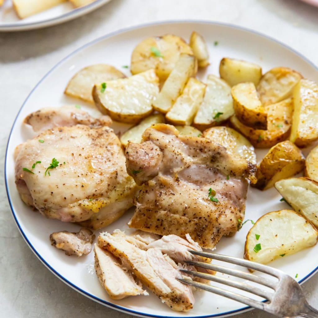 chicken thighs and potatoes on a plate with a fork on the plate