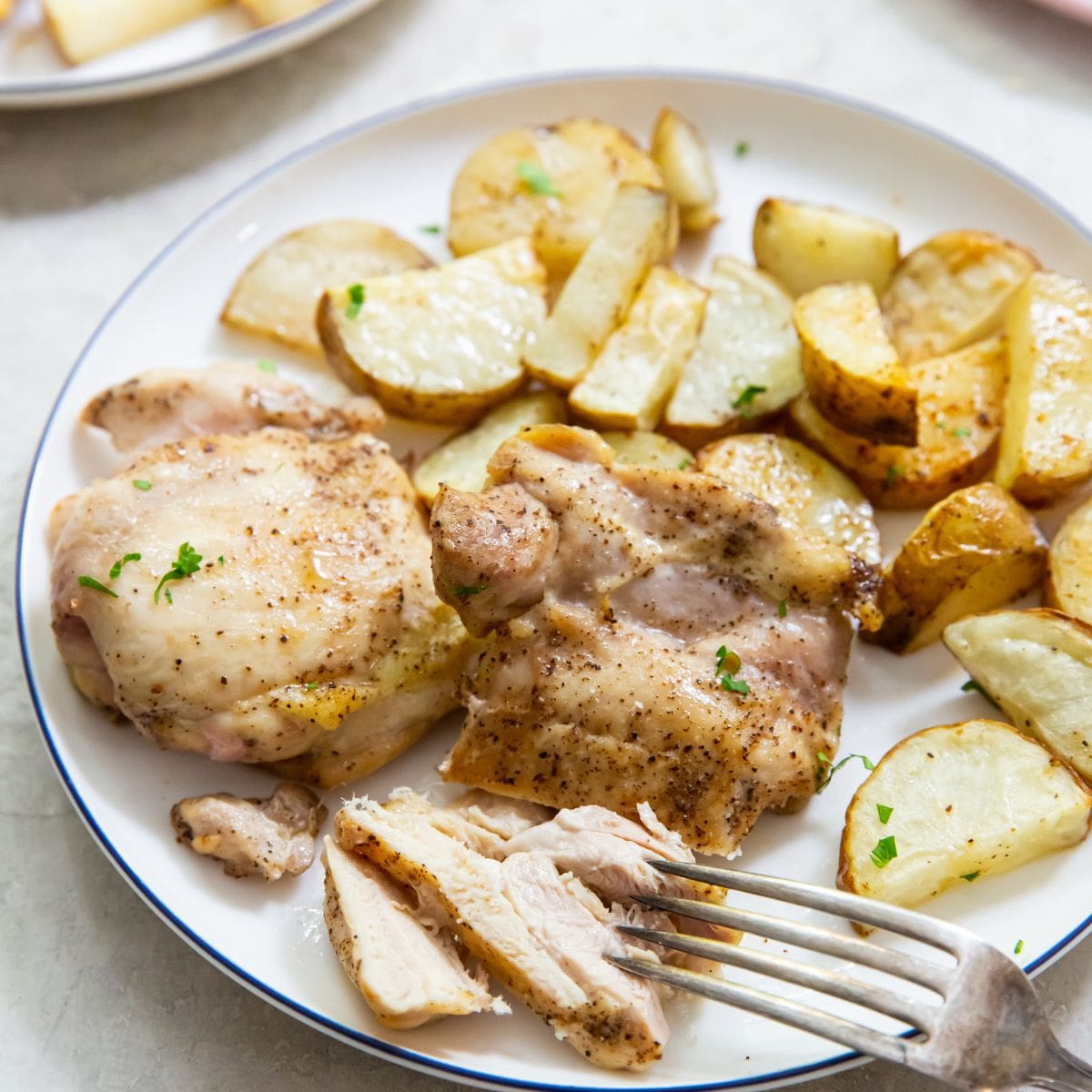 chicken thighs and potatoes on a plate with a fork on the plate