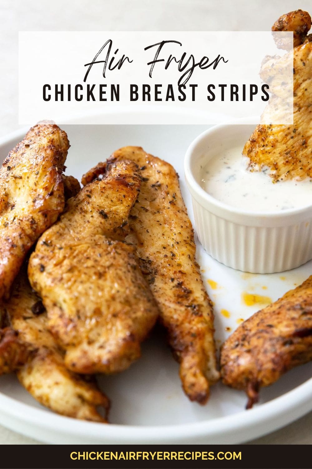 Gray background with white plate chicken breast tenders. One dipped into a side dish of ranch