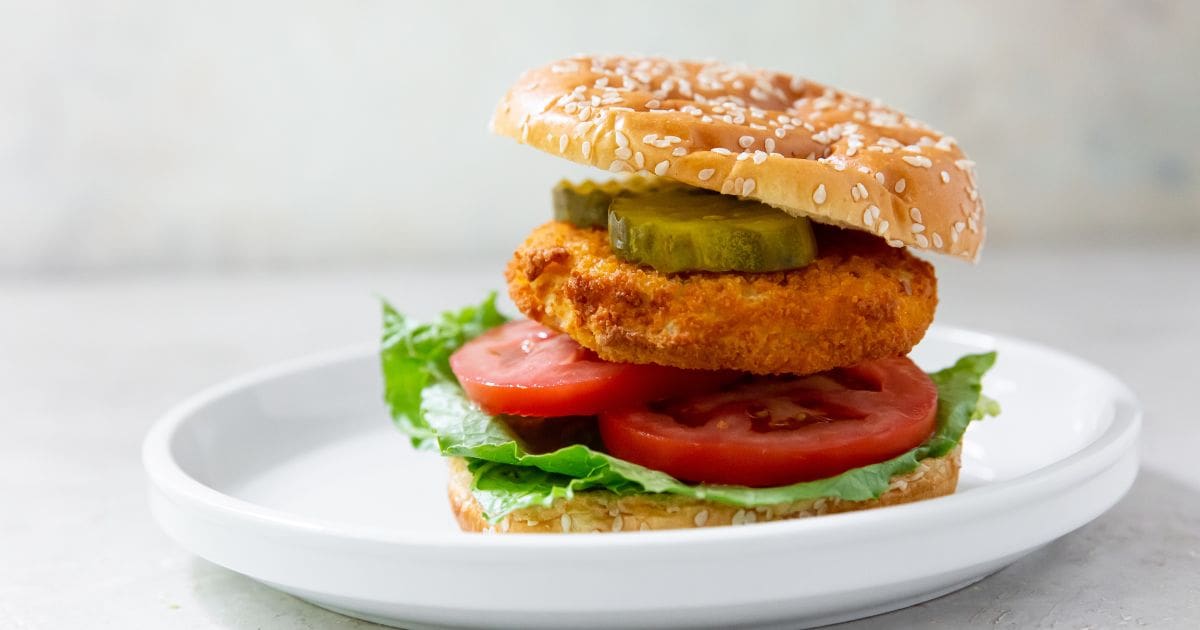 chicken patty with lettuce, tomato and pickles on a white plate