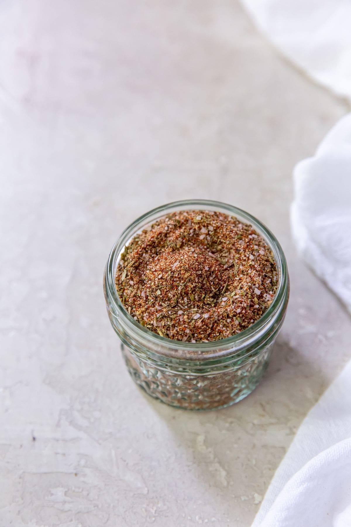 Mason jar with air fryer chicken dry rub seasoning inside. White towel on the side