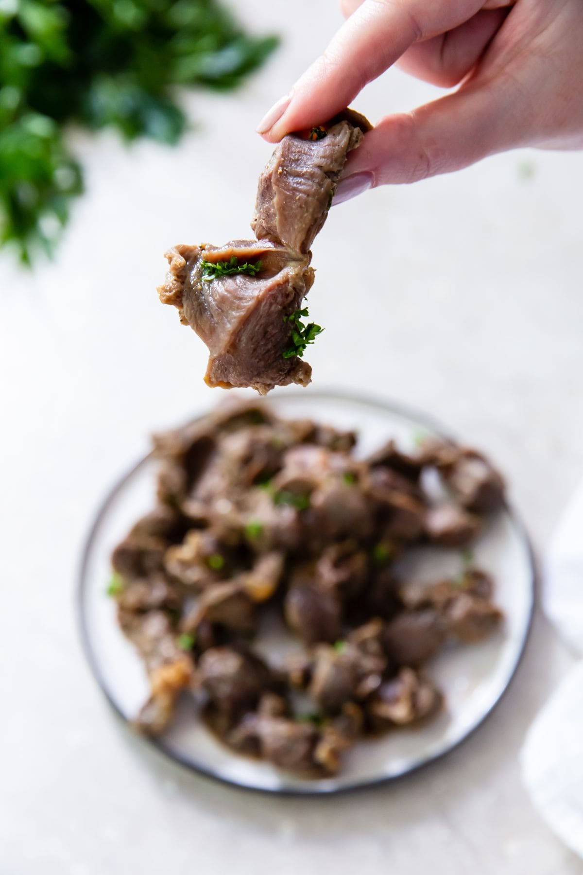 white plate with chicken gizzards. one being held over the plate parsley in the back