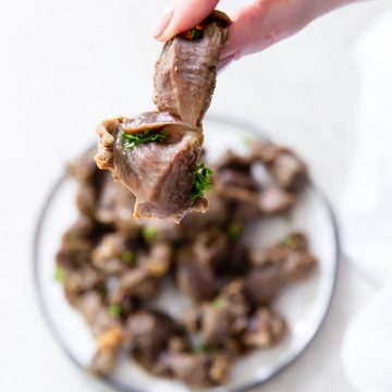 white plate with chicken gizzards. one being held over the plate parsley in the back