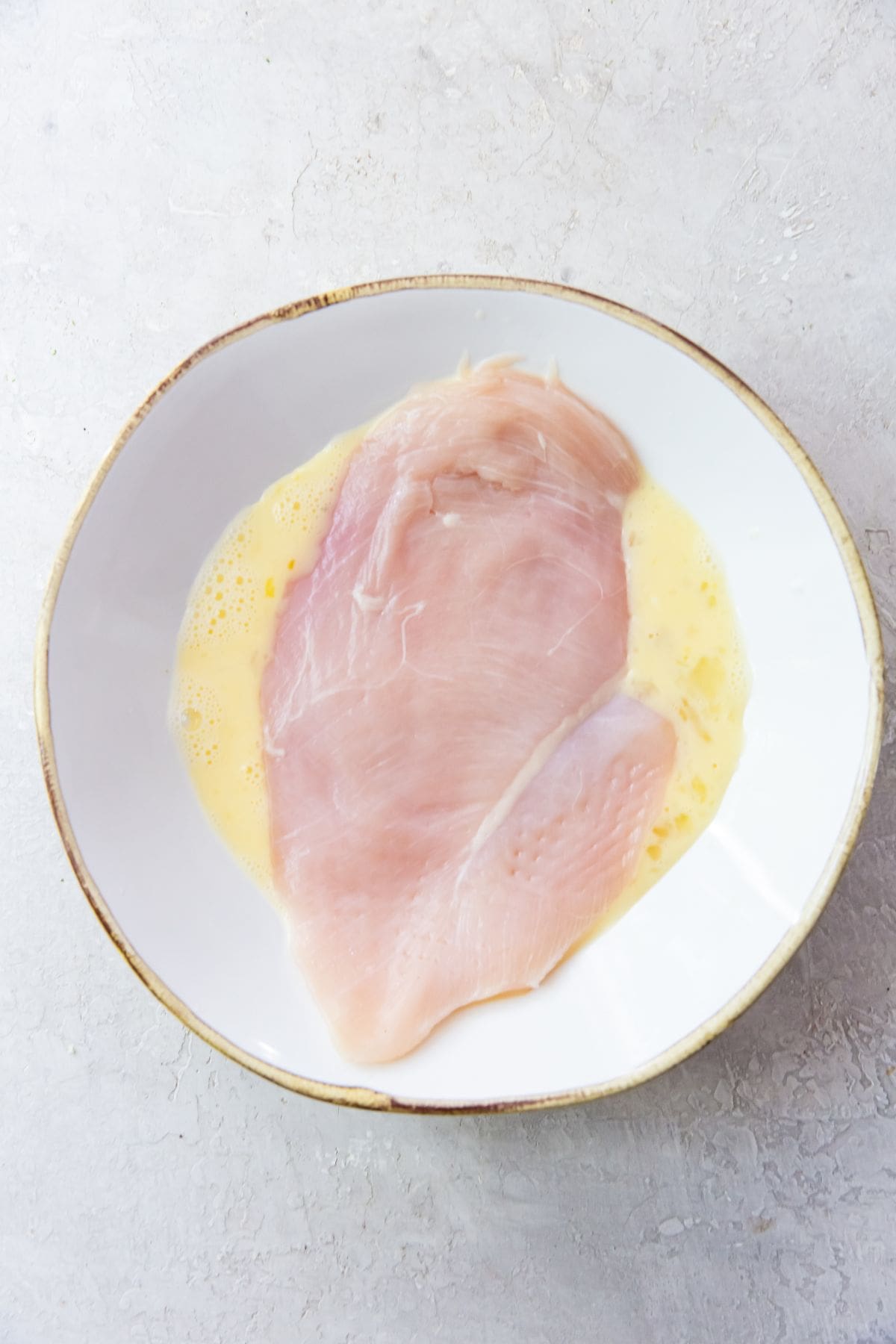 white bowl with chicken breast being dunked into egg bath