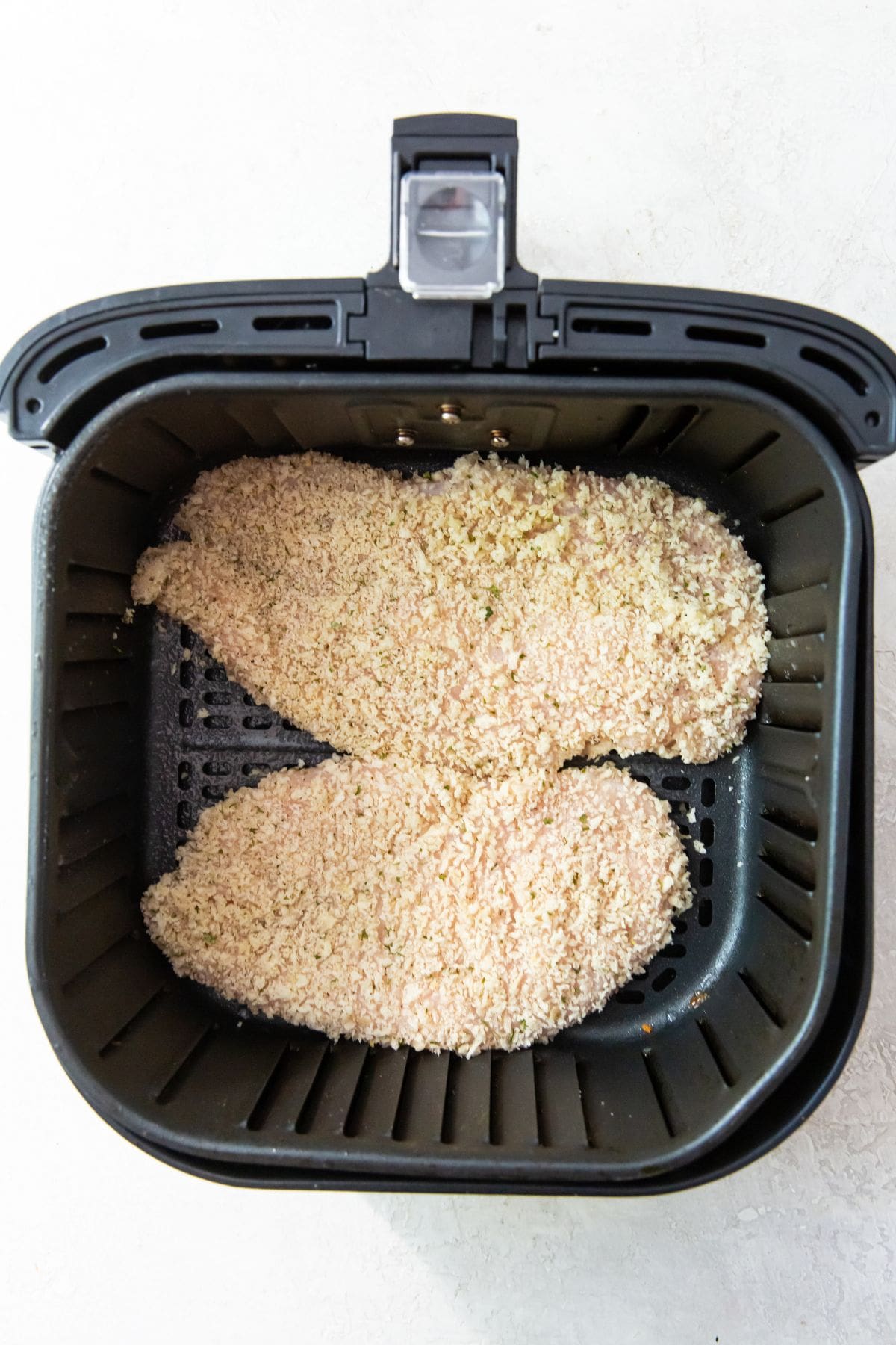 black air fryer with raw chicken inside