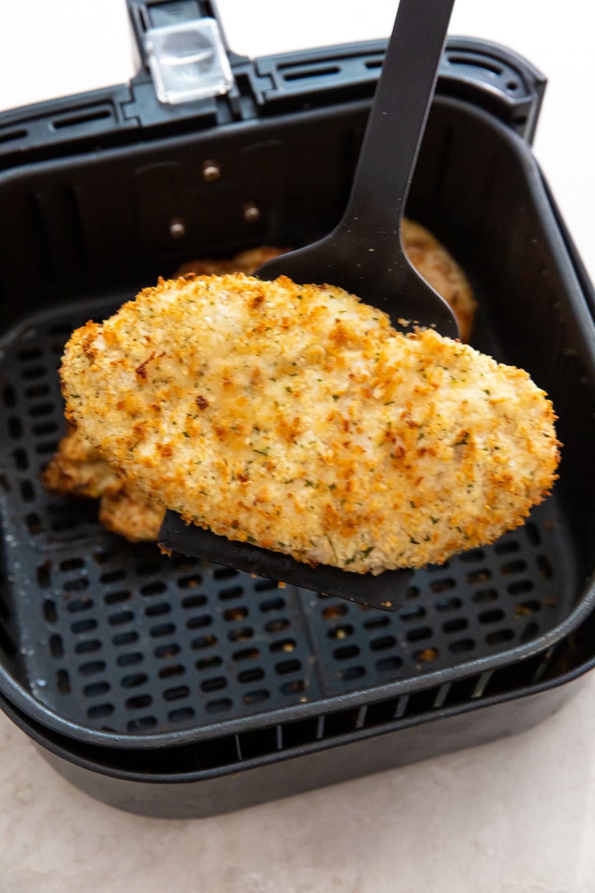 black air fryer with cooked chicken inside about to be flipped