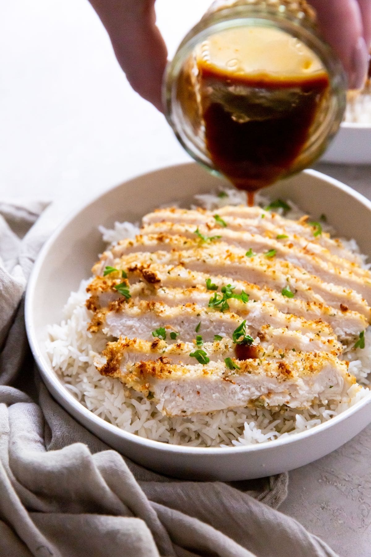 white bowl with air fryer chicken katsu under a bed of rice pouring the katsu sauce on top