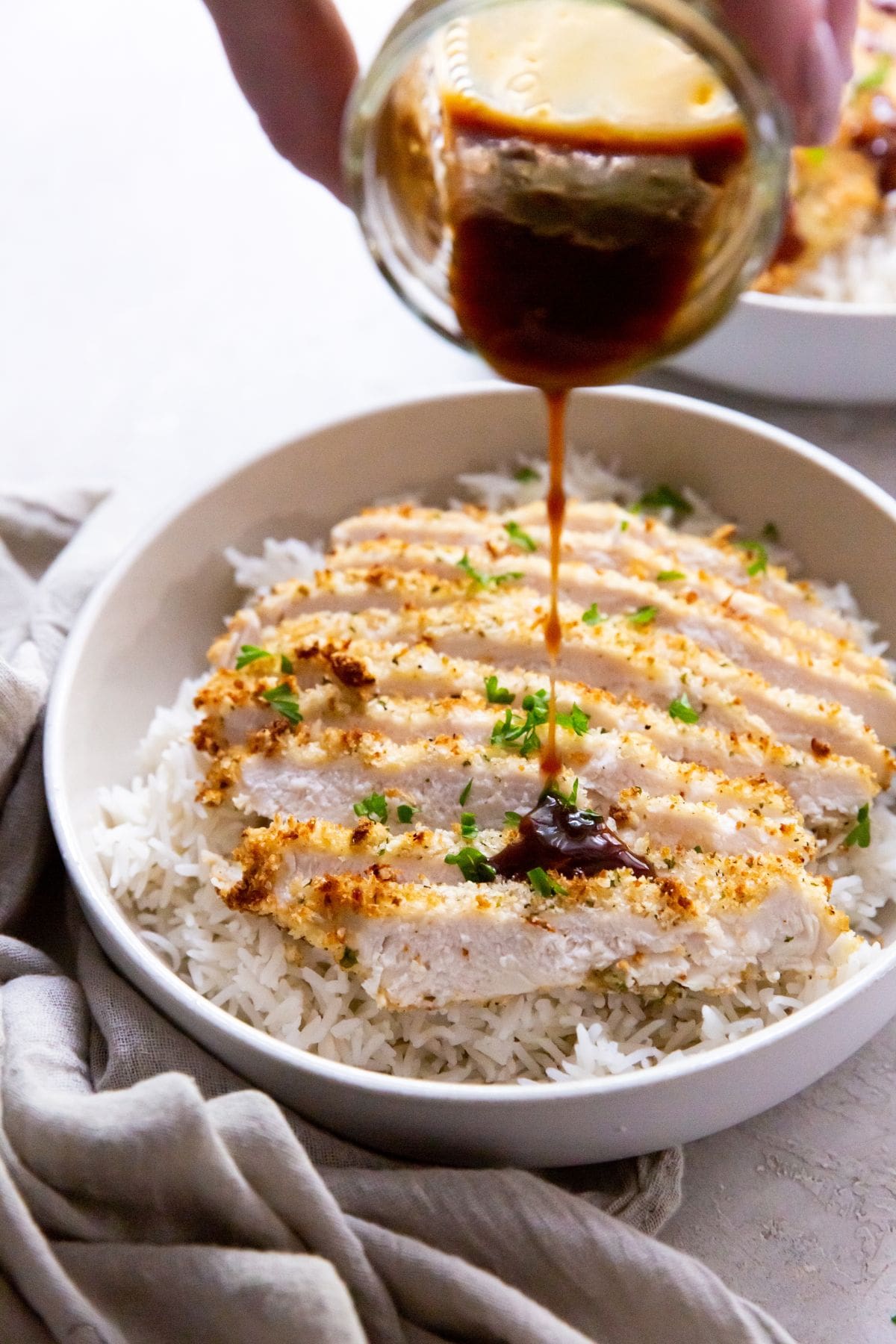 white bowl with air fryer chicken katsu under a bed of rice pouring the katsu sauce on it