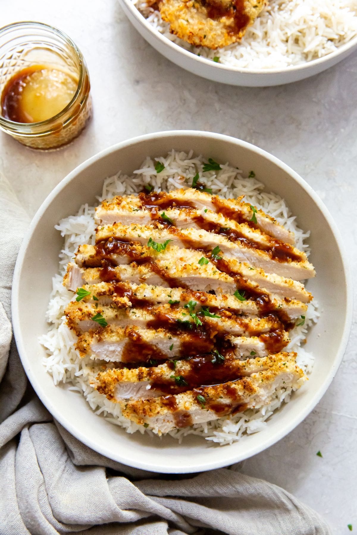 white bowl with air fryer chicken katsu under a bed of rice mason jar behind bowl