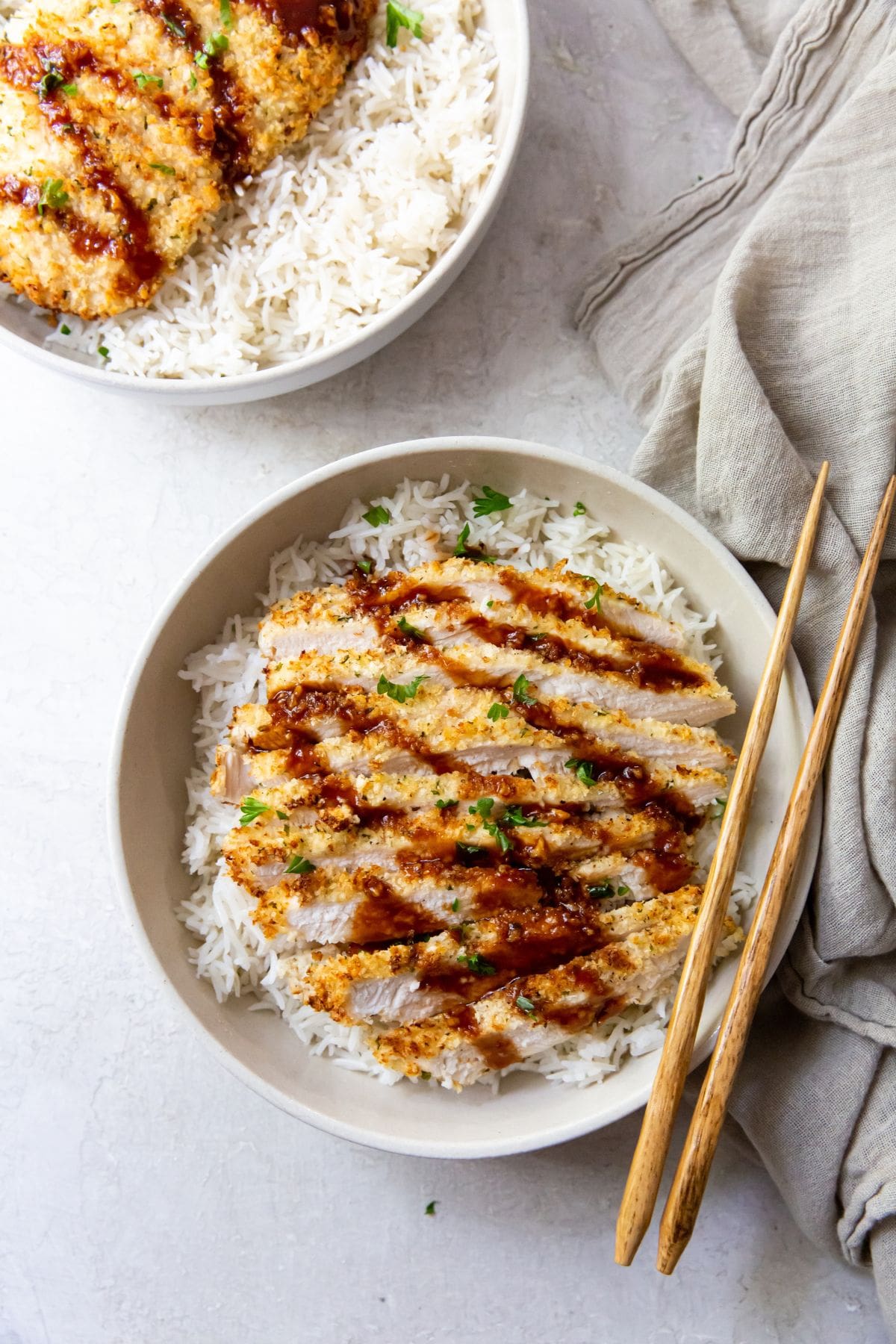 white bowl with air fryer chicken katsu under a bed of rice chopsticks next to it.