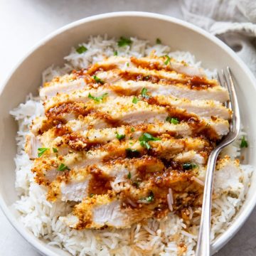 white bowl with air fryer chicken katsu under a bed of rice fork next to it