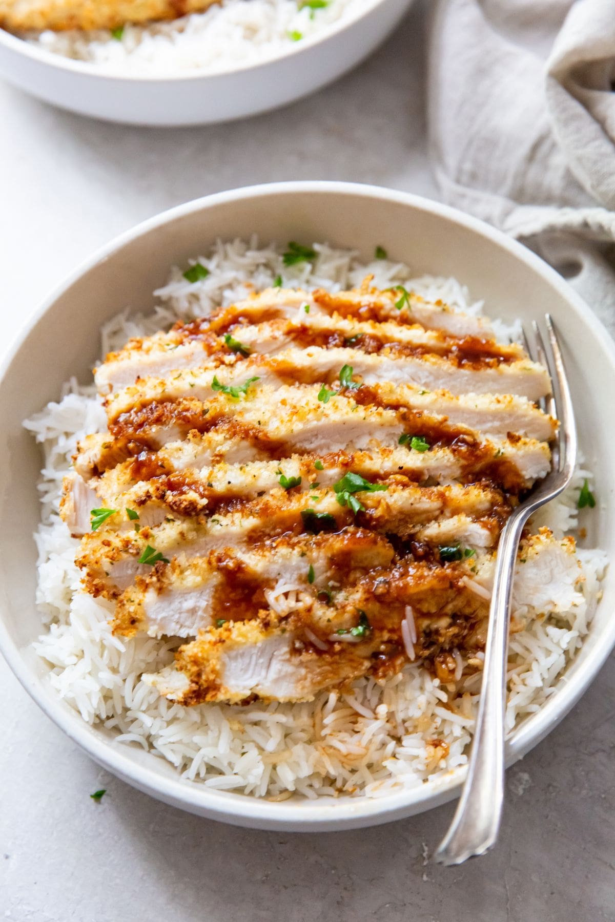 white bowl with air fryer chicken katsu under a bed of rice fork next to it