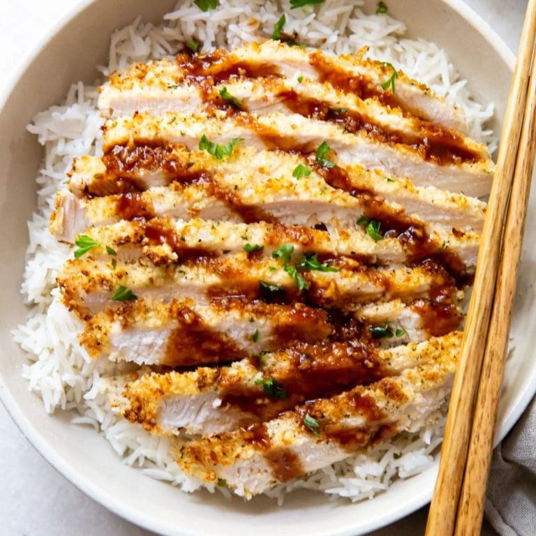 white bowl with air fryer chicken katsu under a bed of rice chopsticks next to it