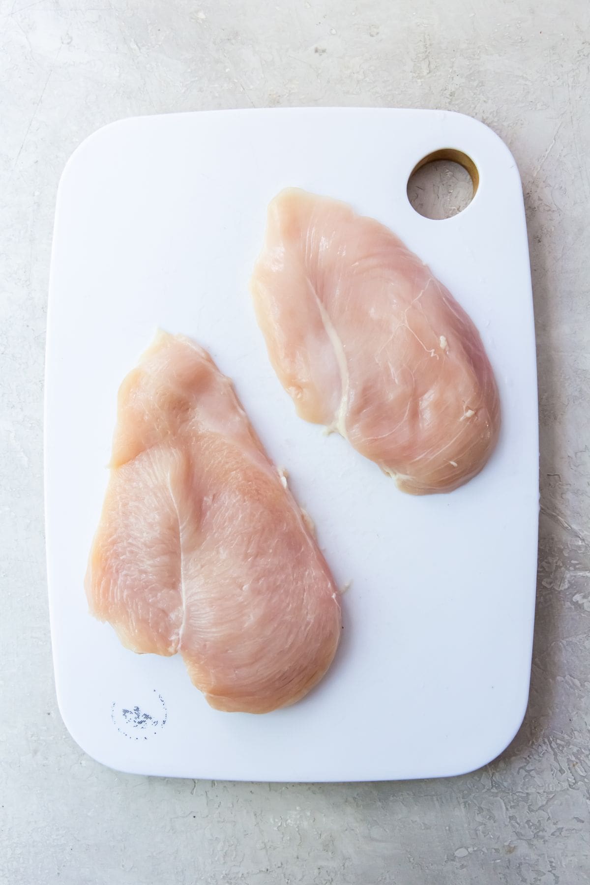 white cutting board with chicken breast