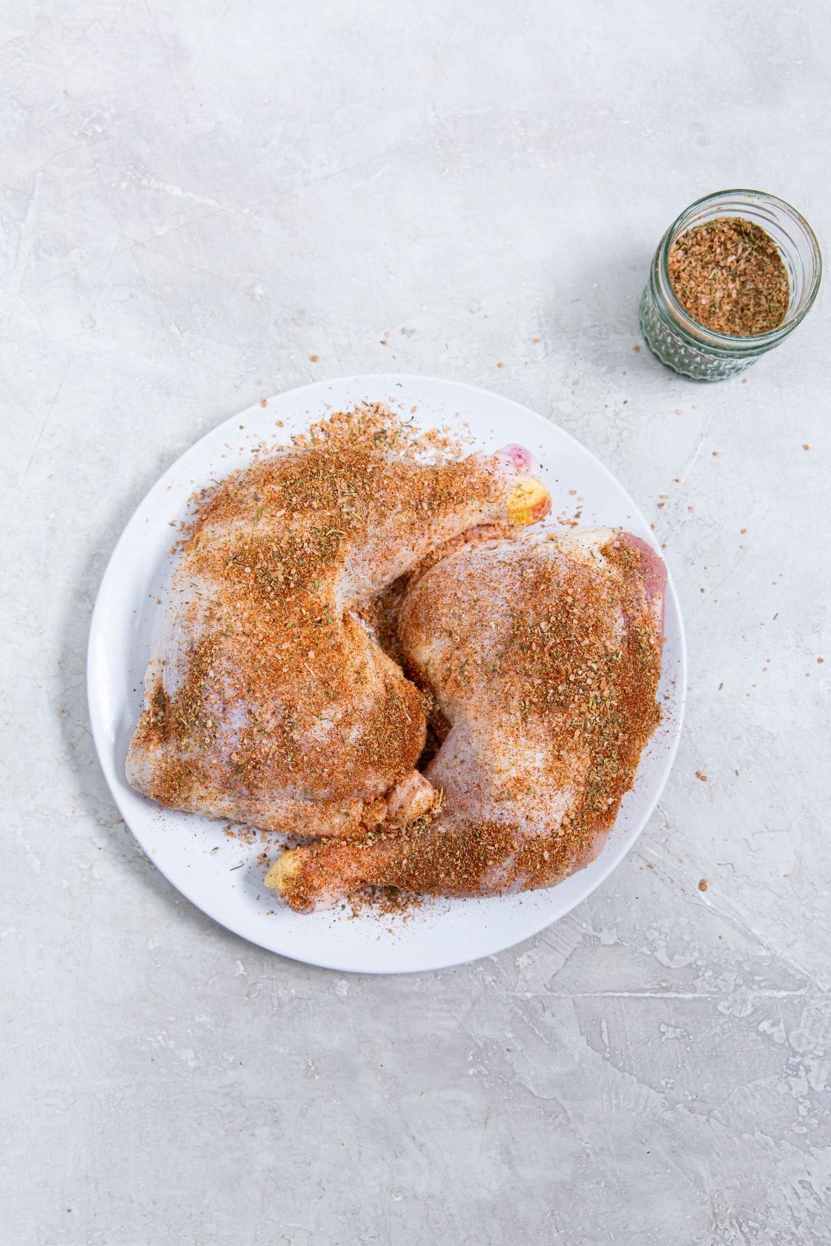 White plate with chicken coated in dry rub seasoning. mason jar of dry rub seasoning