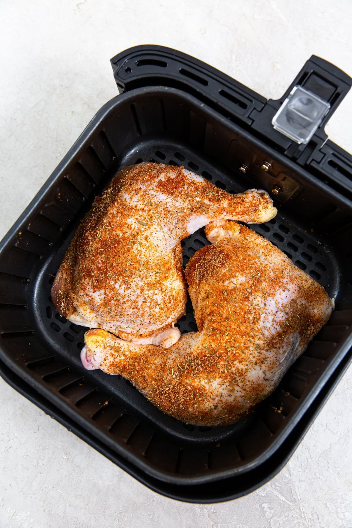 black air fryer with raw chicken leg quarters inside