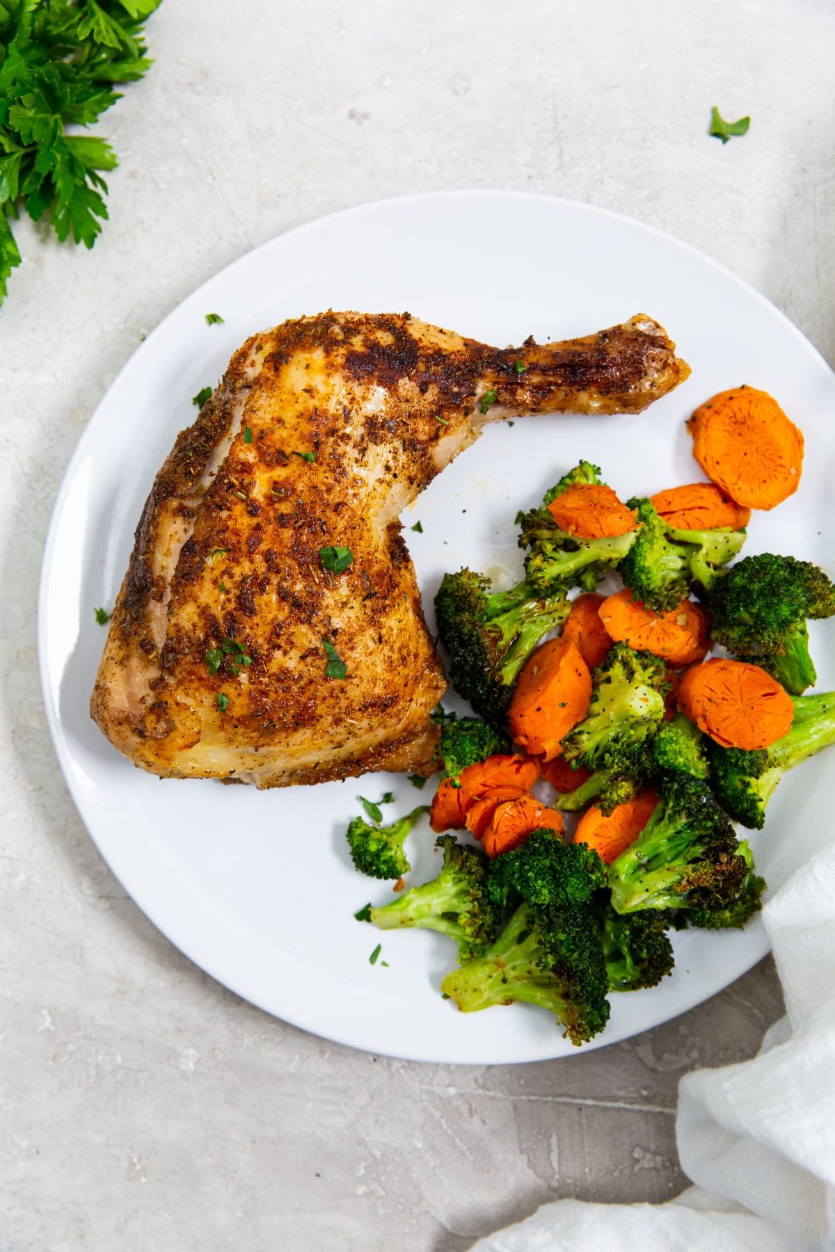 white plate with chicken and vegetables on it parsley in the back. white towel next to it