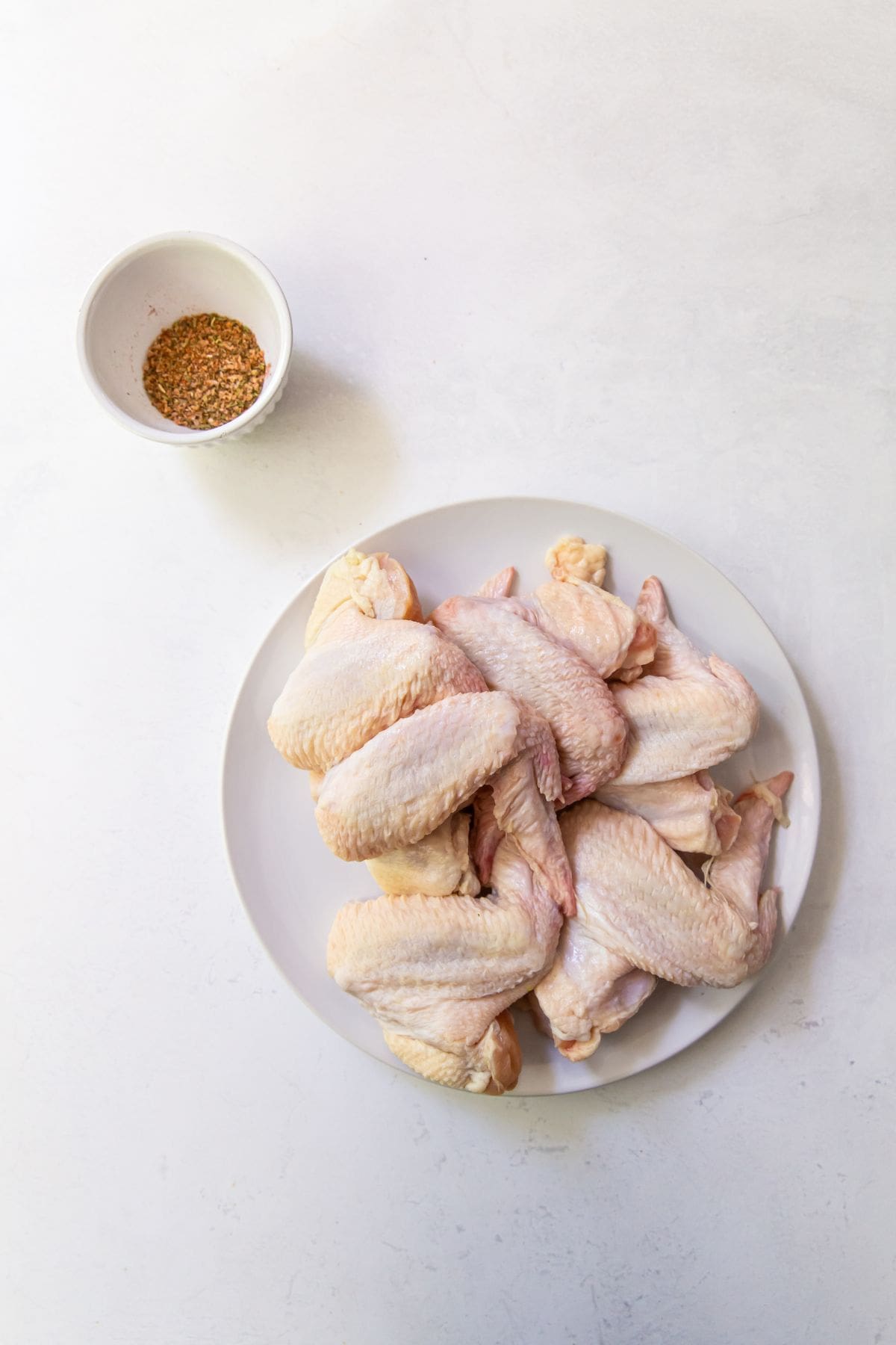 ingredient photo. chicken wings on a plate with dry rub seasoning in a bowl