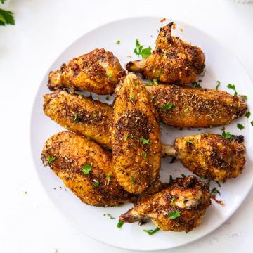 White plate with chicken wings on it. parsley in the back