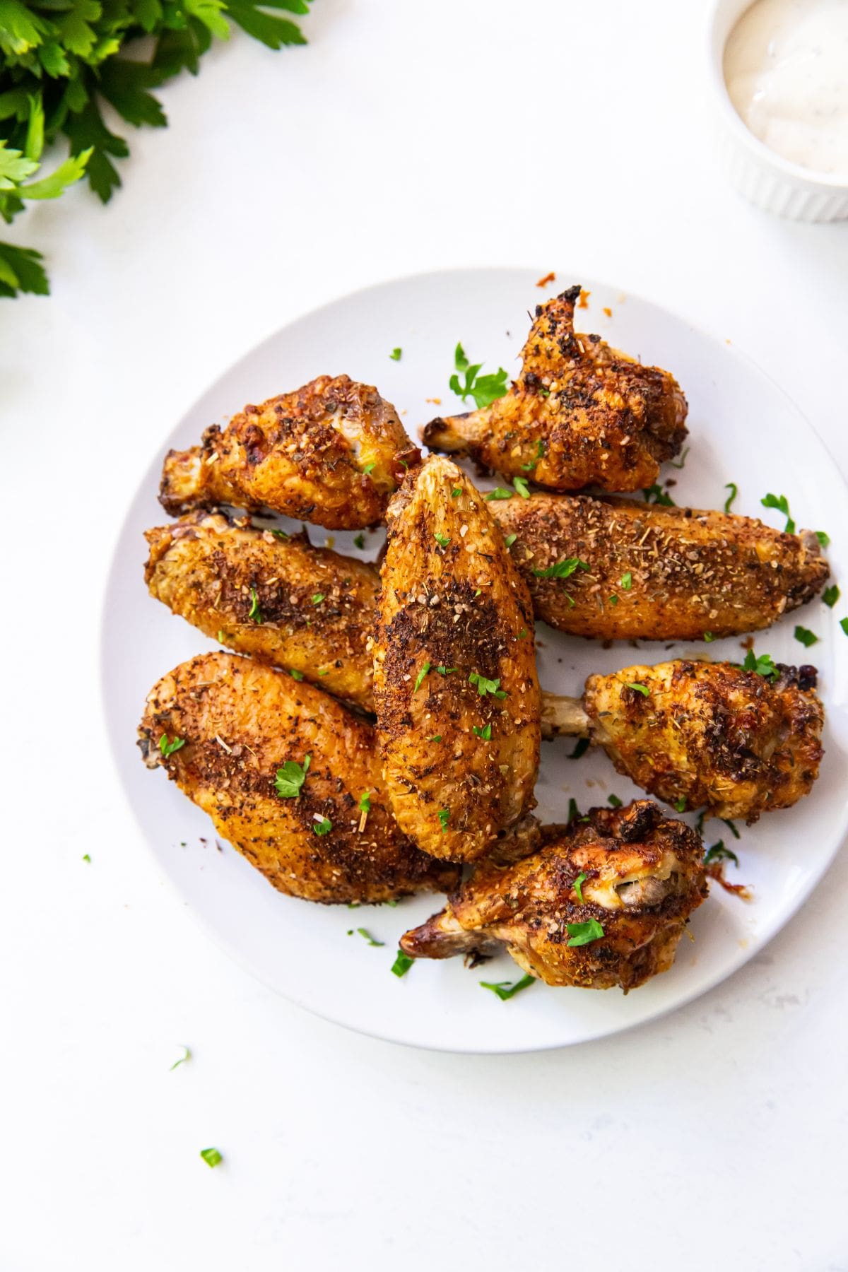 White plate with chicken wings on it. parsley in the back